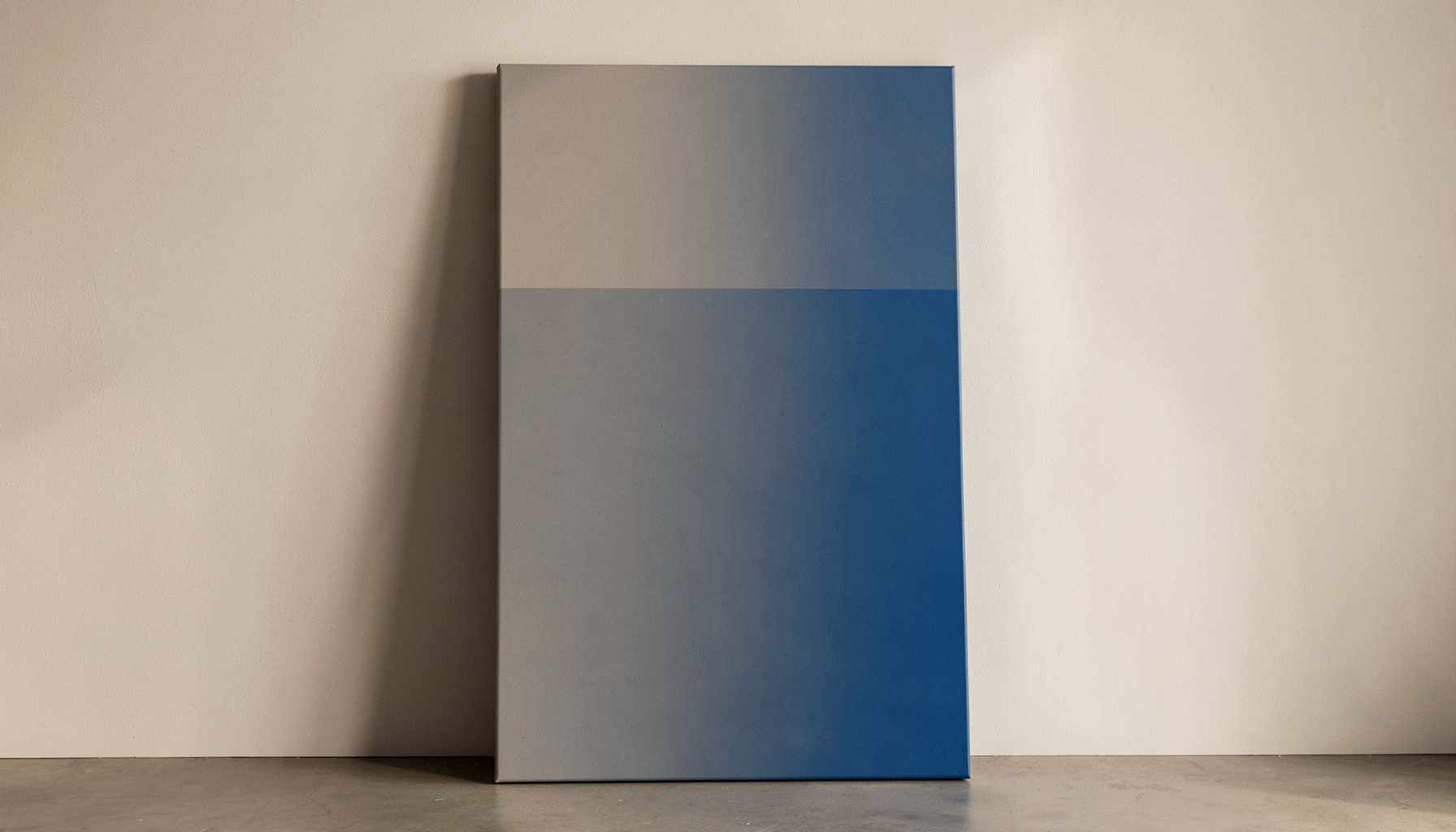 Two-tone duotone photograph of a tall vertical canvas print leaning against a neutral wall, warm taupe and gray palette, gallery mood