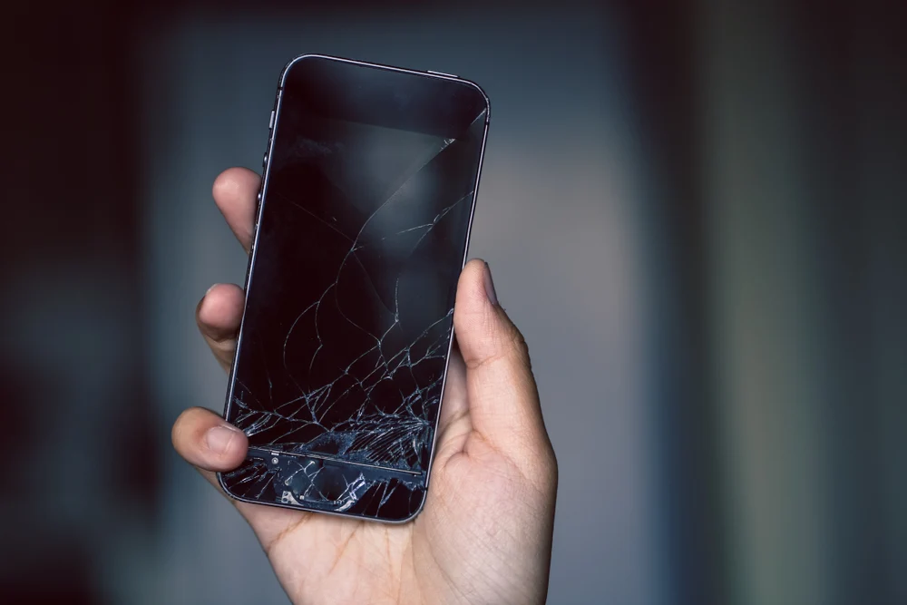 Close-up of a smartphone with a damaged display held in a hand, muted gray and black duotone, mood of wear